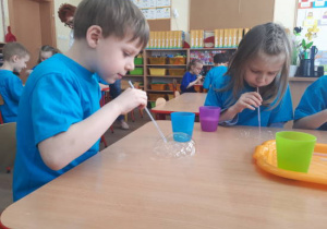 Dwoje dzieci siedzi przy stole podczas zabaw bańkami mydlanymi.